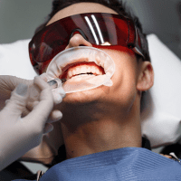 A dentist examining a patient's teeth while wearing a white coat and gloves in a bright dental clinic.