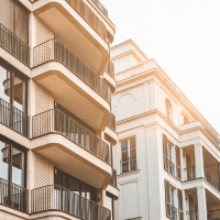An illustration of a modern house with a "For Sale" sign in the front yard, surrounded by trees and a clear blue sky.